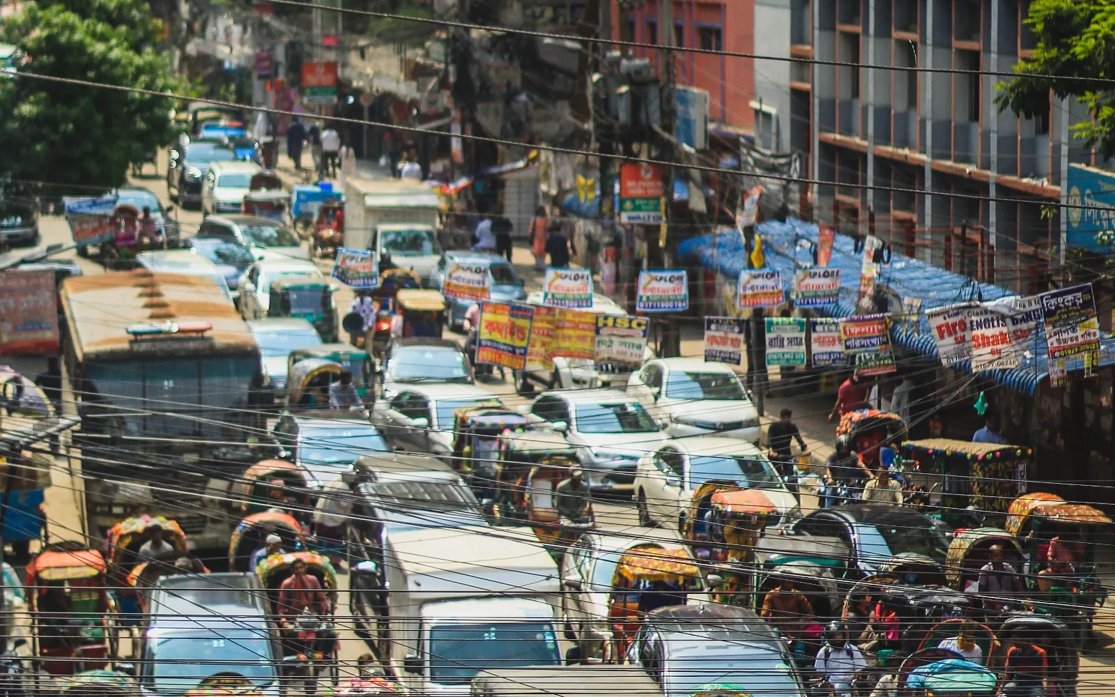 Traffic, roadside commerce and dense development reflect the pressures described in Dhaka.